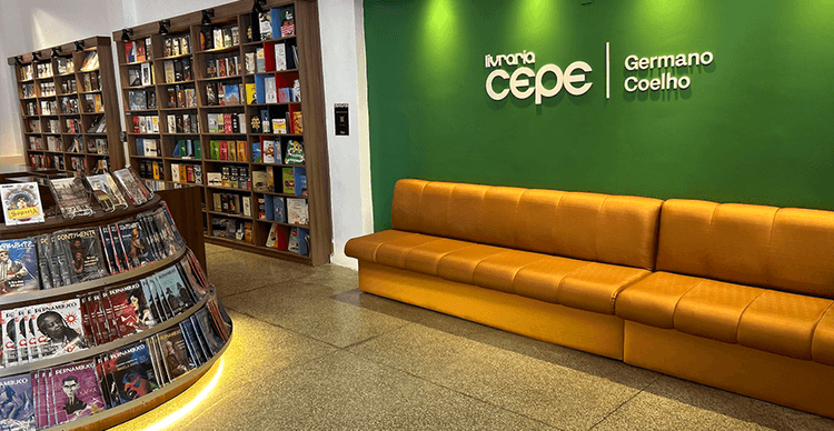 Foto de uma livraria Cepe. Contém estantes com livros, mesas e cadeiras.